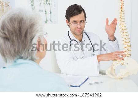 Male doctor explaining the spine to a senior patient in medical office