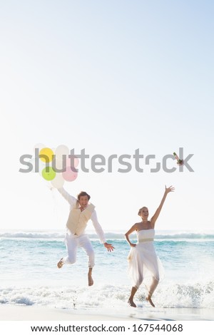 Groom holding balloons and bride throwing her bouquet jumping at the beach