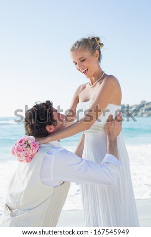 Laughing groom picking up his pretty blonde wife at the beach