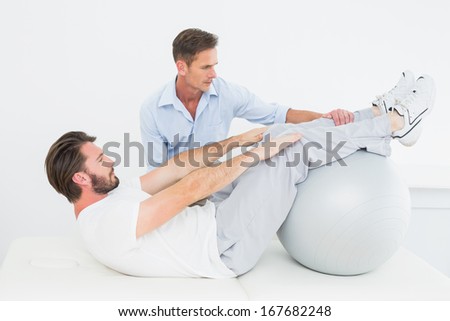 Physical therapist assisting young man do sit ups in the gym at hospital