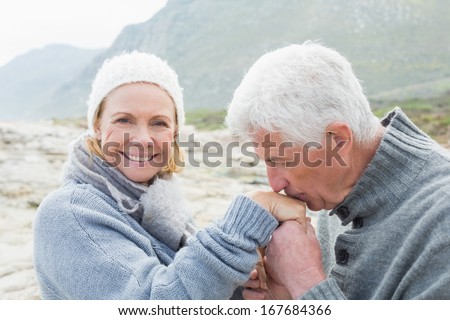 Side view of a senior man kissing happy woman's hand at the rocky beach