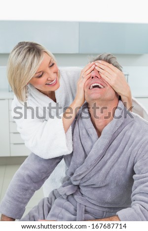Woman covering a happy man\'s eyes from behind in the kitchen at home