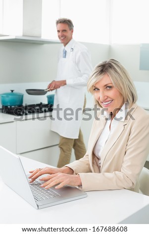 Woman using laptop while man cooking food in the kitchen at home