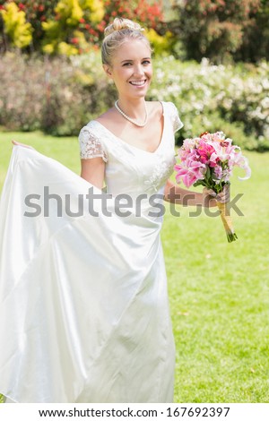 Pretty blonde bride holding lily bouquet and her dress in the countryside