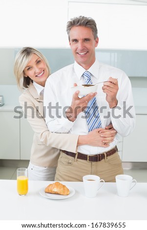 Happy woman embracing man from behind while having breakfast in the kitchen at home
