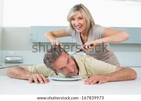 Portrait of a playful woman holding knife to man\'s neck in the kitchen at home