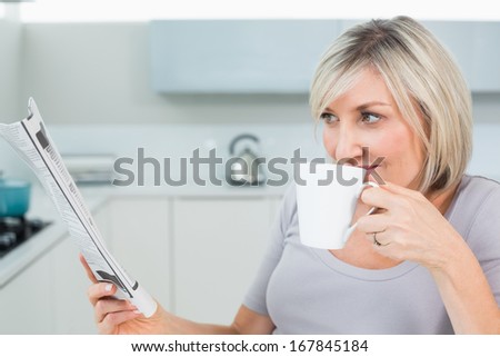 Casual young woman drinking coffee while reading newspaper in the kitchen at home