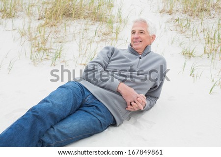 Smiling casual senior man relaxing on sand at the beach