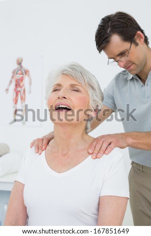 Male physiotherapist massaging a senior woman\'s shoulders in the medical office