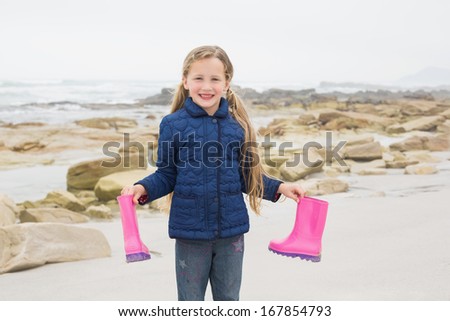 Portrait of a cute smiling young girl holding her wellington boots at the beach