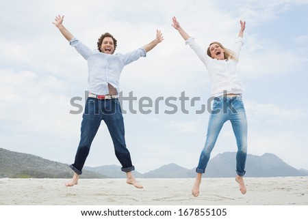 Low Angle View Of A Cheerful Young Couple Jumping At The Beach
