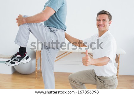 Side view portrait of a male therapist massaging mans lower back while gesturing thumbs up in the gym at hospital