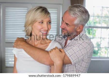 Mature man embracing a happy woman from behind at home