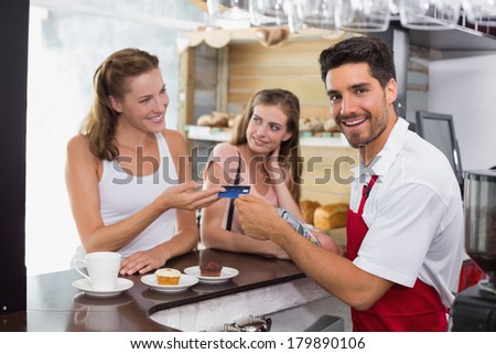 Smiling young female friends paying bill at coffee shop using card bill