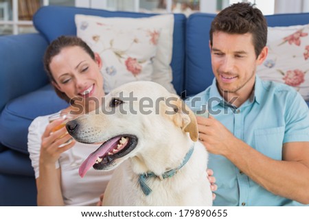 Loving relaxed young couple with wine glasses and pet dog sitting in living room at home