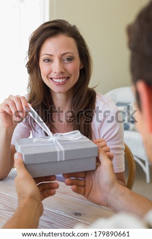 Close-up of a cropped man giving happy woman a gift box at home