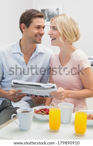 Happy young couple reading newspaper while having breakfast at home