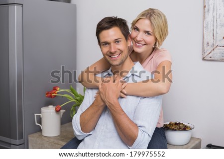 Portrait of a smiling young woman embracing man from behind in kitchen at home