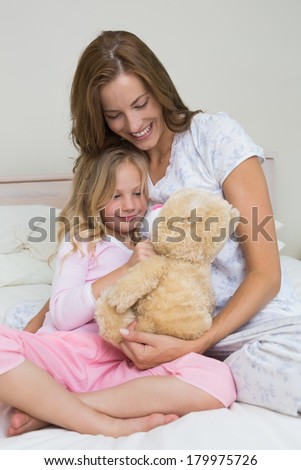 Happy woman and girl playing with stuffed toy in the bedroom at home