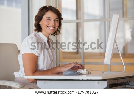Side view portrait of a smiling young businesswoman using computer at office desk