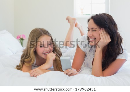 Mother and daughter listening to music on MP3 player while lying in bed at home