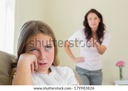 Bored girl with mother scolding her in background at home