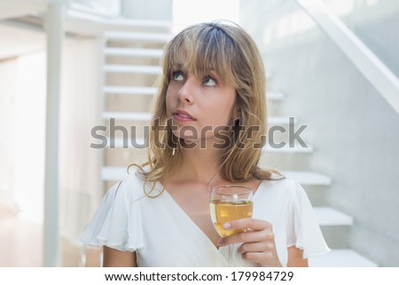 Thoughtful beautiful young woman with wine glass on stairs at home