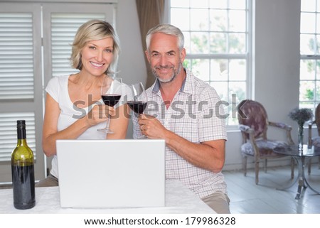 Happy mature couple toasting wine glasses while using laptop at home