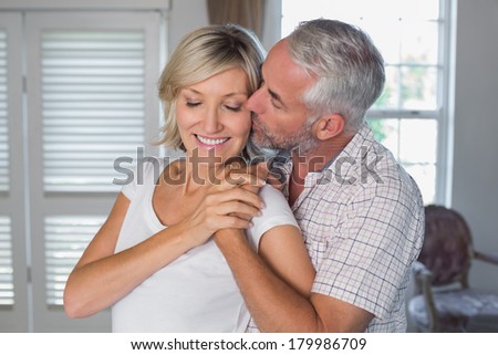 Mature man kissing a happy woman from behind at home