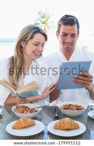 Happy young couple with book and digital tablet on breakfast table at home
