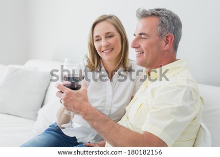 Happy relaxed couple with wine glasses sitting on sofa at home
