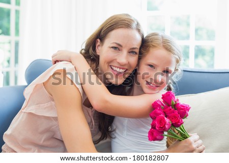 Portrait of a happy mother and daughter embracing with flowers in the living room at home