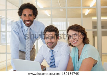 Portrait of three smiling young business people using laptop together at office desk