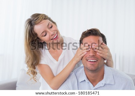 Young woman covering happy mans eyes at home