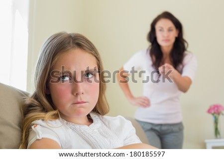 Angry little girl with mother scolding her in background at home