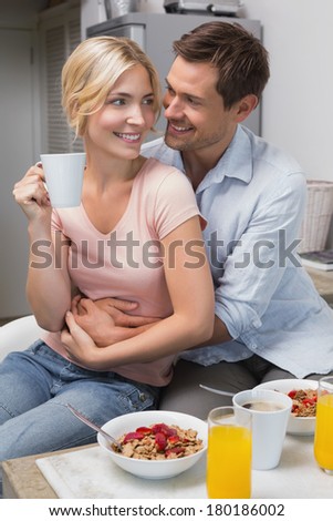 Portrait of a happy young man embracing woman from behind at breakfast table at home
