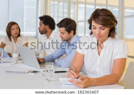 Concentrated young businesswoman writing notes with colleagues in meeting at the office