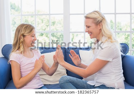 Happy mother and daughter playing clapping game while sitting on sofa at home