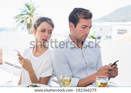 Serious young couple text messaging at food table