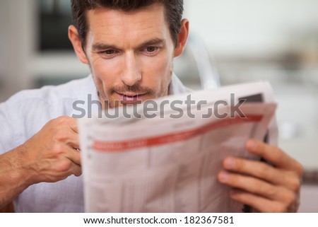 Close-up of a concentrated young man reading newspaper at home