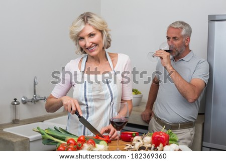 Mature man with wine glass and woman chopping vegetables in the kitchen at home