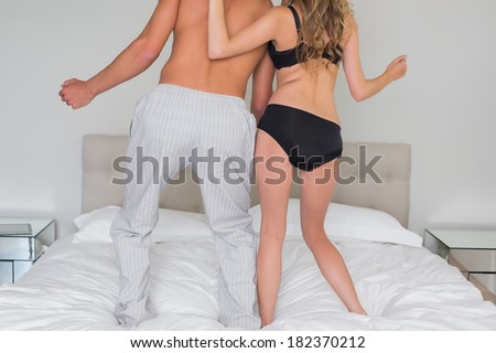 Rear view low section of a semi dressed couple standing on bed at home