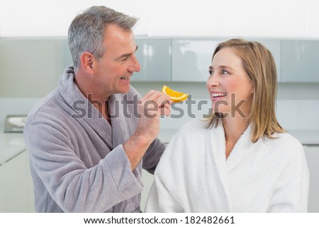 Happy man feeding woman orange slice in the kitchen at home