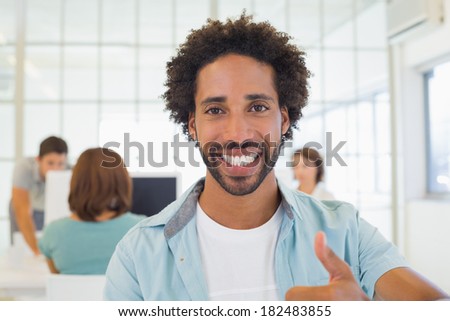 Portrait of a smiling businessman gesturing thumbs up with colleagues in meeting in background at the office