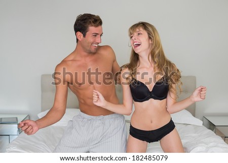 Cheerful semi nude young couple dancing in bed at home