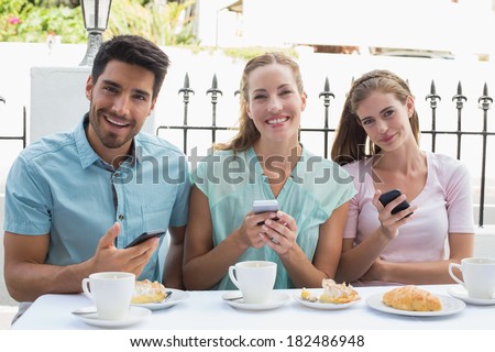 Portrait of three happy friends reading text message in the cafe