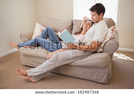 Full length of a relaxed young couple reading book on couch at home