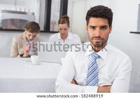 Portrait of confident businessman with colleagues in meeting behind at office desk