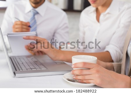Close-up mid section of three young business people using laptop together at office desk