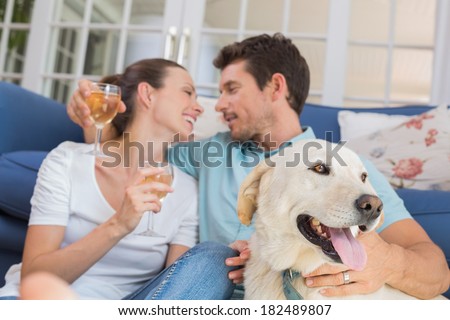 Loving relaxed young couple with wine glasses and pet dog sitting in living room at home